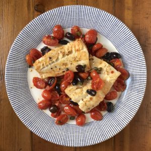 Baked cod with cherry tomatoes and olives on wood table