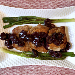 Pork chops topped with cherry sauce and surrounded by charred scallions