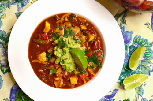 Vegan chili on a yellow, blue, and green tablecloth with a pitcher of sangria mocktail