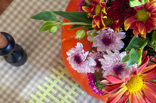 Table with gingham runner and flowers being displayed in a pumpkin with a candle nearby