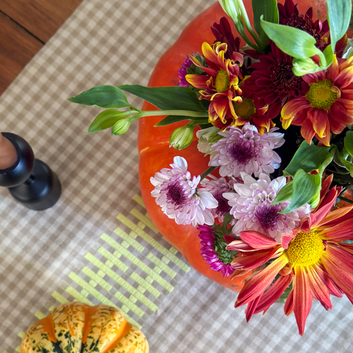 Table with gingham runner and flowers being displayed in a pumpkin with a candle nearby