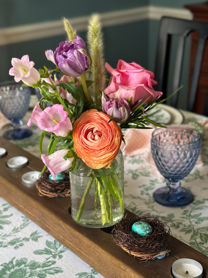 Spring bouquet on an Easter table set with blue glasses and a floral tablecloth