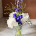 Blue delphiniums and white peonies in a glass vase with green foliage stems