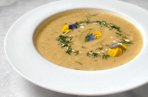 potato leek soup in a white bowl garnished with fresh herbs and edible flower petals