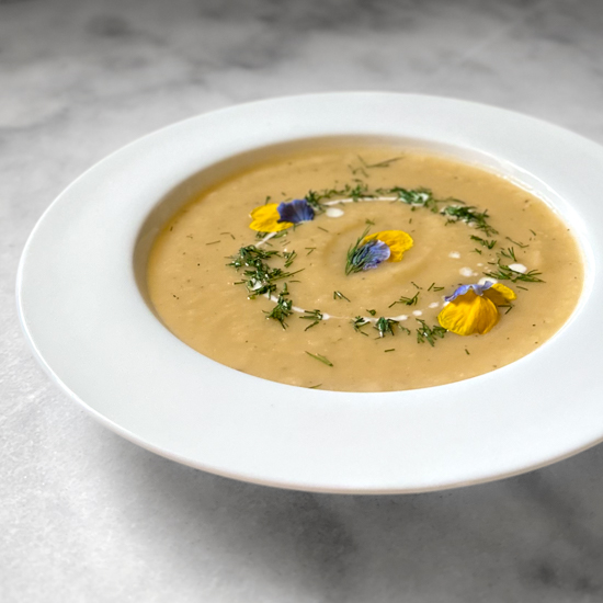 potato leek soup in a white bowl garnished with fresh herbs and edible flower petals