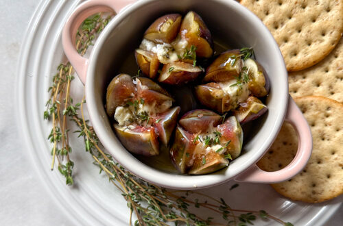 baked figs with cheese, honey and herbs in a ramekin surrounded by crackers