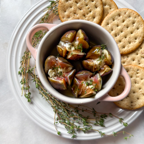 baked figs with cheese, honey and herbs in a ramekin surrounded by crackers